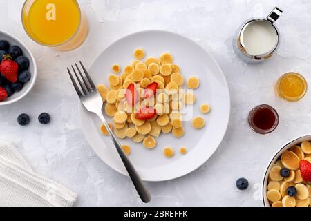 Winziger Mini-Pfannkuchen-Müsli. Hausgemachtes Frühstück mit Himbeeren, Heidelbeeren, Marmelade und Saft auf grauem Hintergrund Stockfoto