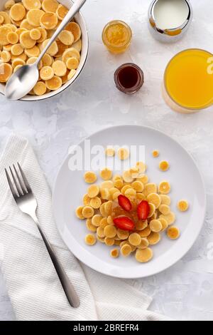 Winziger Mini-Pfannkuchen-Müsli. Hausgemachtes Frühstück mit Himbeeren, Marmelade und Saft auf grauem Hintergrund Stockfoto