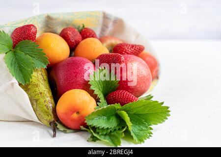 Frisches Obst in einem Bio-Baumwollbeutel auf einem Tisch in der Küche. Mit Äpfeln und Birnen, Aprikosen und Erdbeeren, Zero Waste Trading Konzept. Verbot von Kunststoff Stockfoto