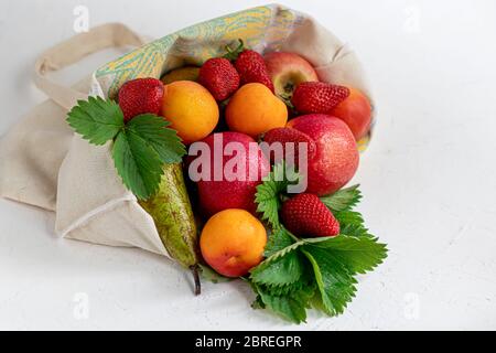 Frisches Obst in einem Bio-Baumwollbeutel auf einem Tisch in der Küche. Mit Äpfeln und Birnen, Aprikosen und Erdbeeren, Zero Waste Trading Konzept. Verbot von Kunststoff Stockfoto