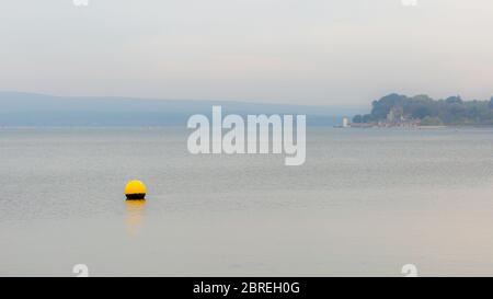 Landschaftsfoto mit Blick auf einen Teil des Poole Harbour mit gelben flachen Wasserboje im Vordergrund und Brownsea Island im Hintergrund an nebligen Tagen. Stockfoto