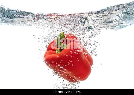 Saftig rot ökologische, Pfeffer fällt in sauberes Wasser erzeugt Blasen. Isoliert auf weißem Hintergrund. Stockfoto