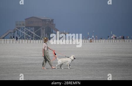 Dpatop - 21. Mai 2020, Schleswig-Holstein, St. Peter Ording: Eine Frau geht mit ihrem Hund auf den kaum besuchten Strand von St. Peter Ording bei strahlendem Sonnenschein spazieren. Normalerweise ist der Strandabschnitt mit Tausenden von Besuchern über Pfingsten gefüllt. Auch am Vatertag ist der Zugang zu den Inseln und nach St. Peter Ording für Tagestouristen im Norden gesperrt. Foto: Axel Heimken/dpa Stockfoto