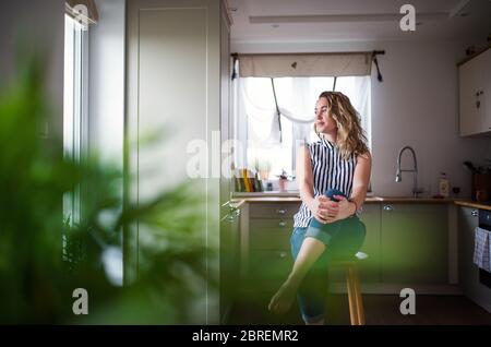 Junge Frau sitzt in der Küche drinnen zu Hause, entspannend. Stockfoto