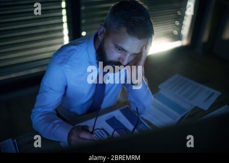 Frustrierter Geschäftsmann mit Computer an der Rezeption, der spät arbeitete. Konzept der Finanzkrise. Stockfoto