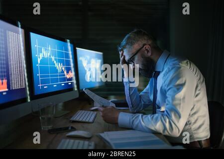 Frustrierter Geschäftsmann mit Computer an der Rezeption, der spät arbeitete. Konzept der Finanzkrise. Stockfoto