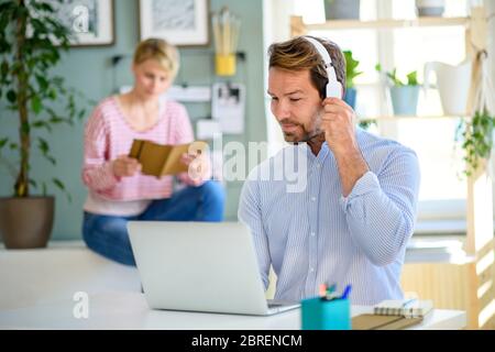 Reifer Geschäftsmann mit Kopfhörern und Laptop im Haus im Büro, arbeiten. Stockfoto