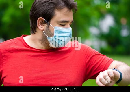Mann mit Gesichtsmaske, der die intelligente Uhr nach den Übungen beobachtet Stockfoto