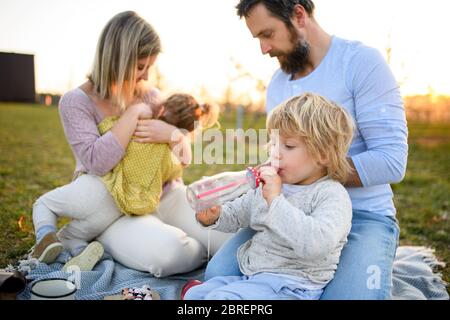 Familie mit zwei kleinen Kindern, die im Frühling bei Sonnenuntergang im Freien picknicken. Stockfoto