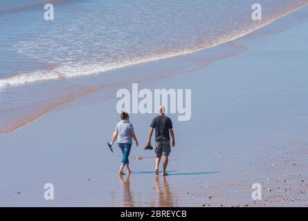 Sidmouth, East Devon, Großbritannien. Mai 2020. UK Wetter: Ein paar gehen barfuß entlang des nassen Sandes und genießen das herrlich heiße und sonnige Wetter in der malerischen Regency Stadt Sidmouth. Die heiße Sonne wird voraussichtlich bis in das Feiertagswochenende der Bank andauern. Quelle: DWRAlamy Live News. Stockfoto