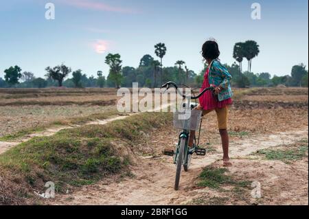 Junge kambodschanische Mädchen auf einem Fahrrad hält auf einer kleinen Spur, um den Sonnenuntergang zu beobachten. Provinz Siem Reap, Kambodscha, Südostasien Stockfoto