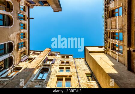 Blick von unten auf den Innenhof des Wohnhauses in Venedig, Italien. Geometrisches Panorama des alten Wohngebäudes mit blauem Himmel. Hof-gut in Stockfoto
