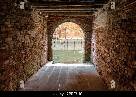 Ausgang zum Wasserkanal vom Hof, Venedig, Italien. Vintage-Korridor von Hof von Wohnhäusern. Alte Architektur von Venedig. Alte Straße von t Stockfoto