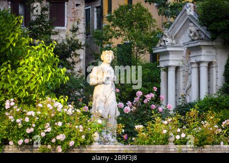 Panoramalicht auf eine Straße in Venedig, Italien. Alte Häuser mit schönem Garten am Canal Grande im Zentrum von Venedig. Klassische Marmorstatue im Blumengarten Stockfoto