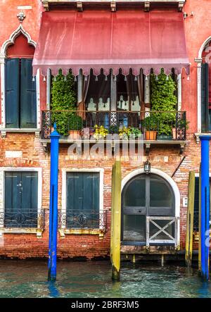 Alte rote Fassade in Venedig, Italien. Vorderansicht des Gebäudes mit Eingang in Venedig. Vintage Hotel oder Wohnhaus am Wasser. Alt Stockfoto