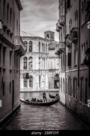 Venedig in schwarz-weiß, Italien. Alte schmale Straße mit einiger Gondel in der Ferne. Romantische Wassertour über die alten Kanäle Venedigs. Konzept der tr Stockfoto