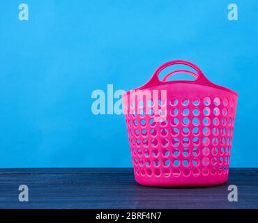 Kunststoff rosa Korb im Loch für saubere und schmutzige Wäsche, Kleidung auf blauem Hintergrund, Behälter, Kopierraum Stockfoto