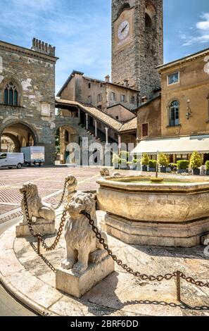 Bergamo im Sommer, Italien. Piazza Vecchia in Citta Alta oder Upper City. Löwenstatuen mit Ketten am alten Brunnen im alten Bergamo Zentrum. Stockfoto