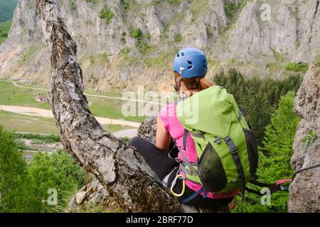 Frau hoch oben auf einem Klettersteig namens 'Spirala Mare' in Baia de Fier, Gorj County, Rumänien, blickt in der Ferne, sitzt neben einem Baum t Stockfoto