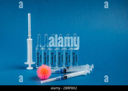 Abstraktes Modell von Coronavirus, Spritzen und Ampullen mit Medizin auf blauem Hintergrund. Die Ampulle enthält einen Coronavirus-Impfstoff. Coronavirus stoppen. Epidemie, Rettungs-Impfstoff. Stockfoto