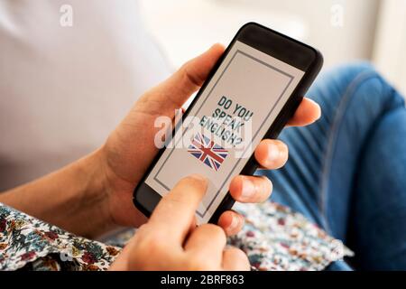 Nahaufnahme eines jungen kaukasischen Mannes, der lässige Kleidung trägt, drinnen auf einer Couch sitzt, sein Smartphone in den Händen hat mit dem Text do you speak en Stockfoto