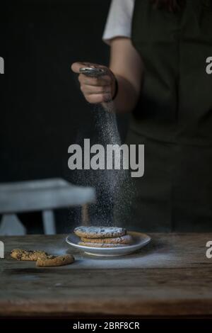 Hand streuen Puderzucker auf Kekse auf einem Holztisch Stockfoto