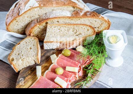 In Scheiben geschnittenes hausgemachtes Brot, frischer Jamon, Oliven und hartgekochtes Ei für einen Snack oder Frühstück auf dem hölzernen Küchentisch. Stockfoto