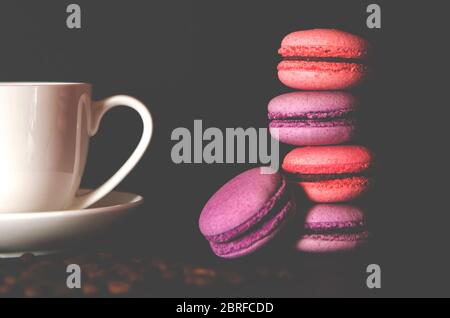 Macarons mit einer weißen Tasse Kaffee auf schwarzem Hintergrund. Stockfoto