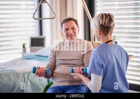 Ein Mitarbeiter im Gesundheitswesen und ein älterer Patient im Krankenhaus, der Sport macht. Stockfoto