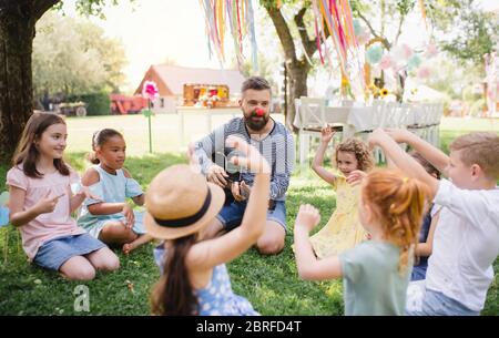 Mann mit kleinen Kindern auf dem Boden im Garten im Sommer, Gitarre spielen. Stockfoto