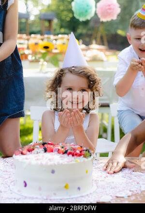 Kleines Mädchen mit Kuchen Geburtstag im Garten im Sommer feiern, Party-Konzept. Stockfoto