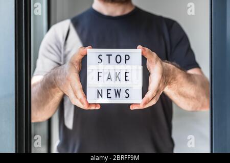 Fake News Infosemics during Covid-19 Pandemie Concept. Mann Hände halten Leuchtkasten mit Text Stoppen Fake News im Vordergrund. Die Leute wollen den Trut kennen Stockfoto
