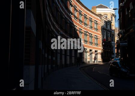 Ein Mann geht entlang einer gebogenen Straße in der City of London mit einem Schaft von Nachmittagslicht. Fotografie von DFphotography.co.uk/Danny Fitzpatrick Credit Stockfoto
