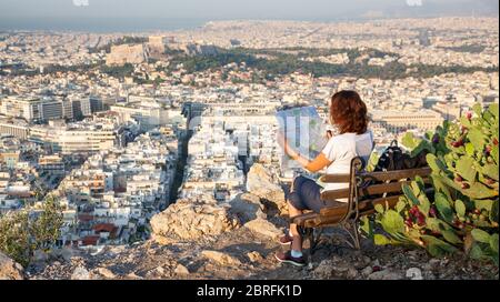 Frau mit einer Karte auf dem Lycabettus-Hügel, dem höchsten Punkt der Stadt mit Blick auf Athen mit der Akropolis - Weltreisender Stockfoto