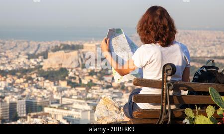 Frau mit einer Karte auf dem Lycabettus-Hügel, dem höchsten Punkt der Stadt mit Blick auf Athen mit der Akropolis - Weltreisender Stockfoto