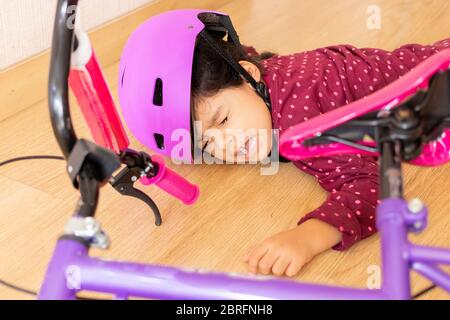 Trauriges kleines Mädchen fiel auf den Boden, während sie mit ihrem Fahrrad im Haus spielte Stockfoto