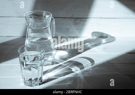 Schatten aus der Karaffe und ein Glas Wasser auf weißem Holzhintergrund Stockfoto