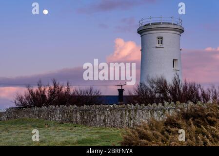 Ein hockes, weißes turmähnliches Gebäude, in ländlicher Lage, gegen einen rosa gefärbten Abendhimmel, mit dem Mond deutlich sichtbar am Himmel Stockfoto