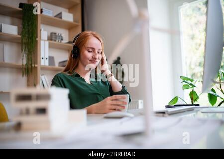 Junge Geschäftsfrau mit Kopfhörer sitzt am Schreibtisch im Büro. Stockfoto