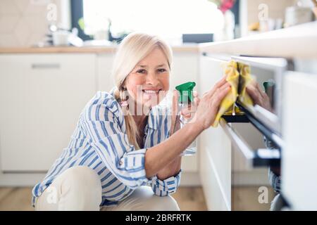 Porträt von älteren Frau Reinigung Küchenschranktüren im Haus. Stockfoto