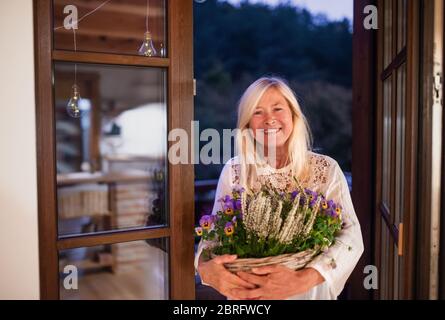 Ältere Frau mit Blumen im Korb im Freien auf der Terrasse. Stockfoto