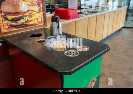 Nahaufnahme von verschiedenen Einweg-Holzstäbchen, Plastikutensilien, Gewürze, Zahnstäbchen und Zuckersäcke auf Holztheke im Café für Selbstbedienung und Stockfoto