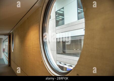 Große runde Fenster auf einer grauen Betonwand in einer geraden Reihe. Ein weiteres modernes Gebäude kann durch das Fenster gesehen werden. Stockfoto
