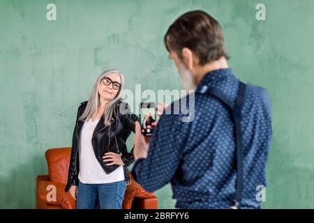 Porträt von schönen älteren Mann, der Foto von seiner schönen niedlichen schönen grauen haarige Frau posiert vor der Kamera und lächelt. Ältere Paare haben Spaß Stockfoto