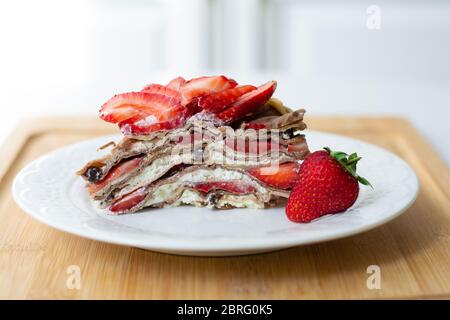 Leichtes Sommerdessert: Eine Scheibe Crepe Layer Kuchen mit Schlagsahne, Schokoladenchips und Erdbeeren zwischen den Schichten. Stockfoto