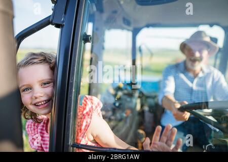 Senior Farmer mit kleinen Enkelin sitzt im Traktor, fahren. Stockfoto