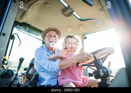 Senior Farmer mit kleinen Enkelin sitzt im Traktor, fahren.
