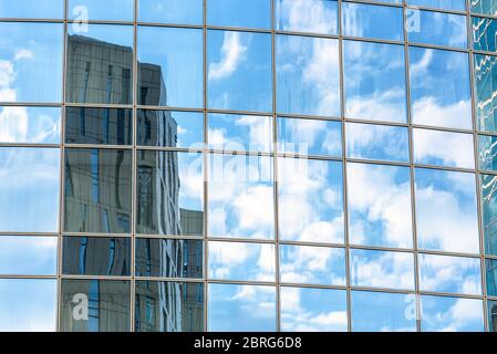 Abstrakter Architekturhintergrund. Himmel und Gebäude spiegeln sich in der Bürohochhaus-Fassade wider. Konzept der modernen städtischen Konstruktionen und Wirtschaft. Stockfoto