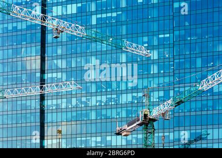 Baukräne auf dem Hintergrund des modernen Gebäudes. Glasfassade des Wolkenkratzers auf der Baustelle. Stockfoto