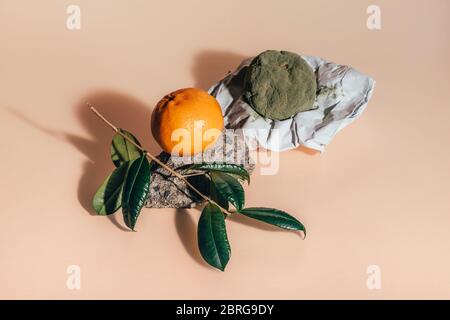 Frische und verfaulte Mandarinen. Verwöhnte Mandarinen mit grünem Schimmel und Pilz auf Papier und eine reife frische auf einem Felsen mit grünem Ast mit Blättern auf korallenfarbenem Hintergrund. Stockfoto